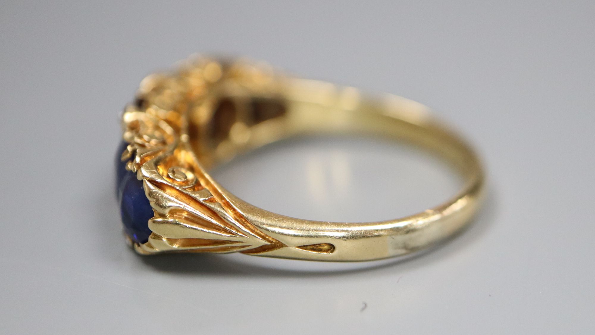 A George V 18ct gold and graduated five stone sapphire set half hoop ring, with diamond chip spacers,